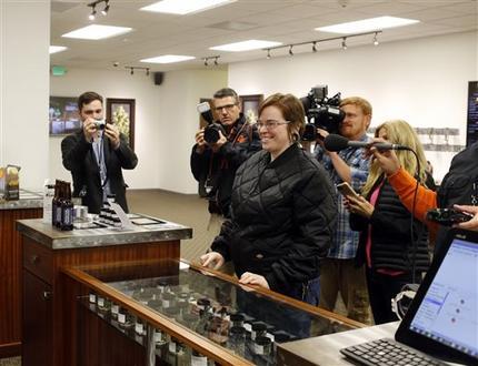 Davia Fleming, 29, center, is surrounded by media members as she becomes the first shopper at Shango Premium Cannabis, in Portland, Ore. On Oct. 1, 2015. Oregon marijuana stores have begun sales to recreational users. (AP Photo/Timothy J. Gonzalez)