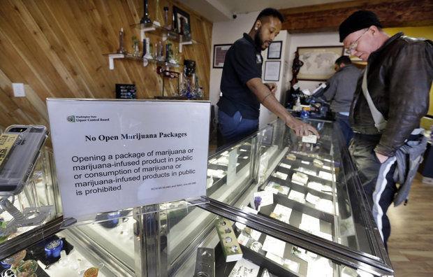 Cannabis City clerk Will Bibbs, left, helps a customer looking over a display case of marijuana products at the shop in Seattle. (AP Photo/Elaine Thompson, File)