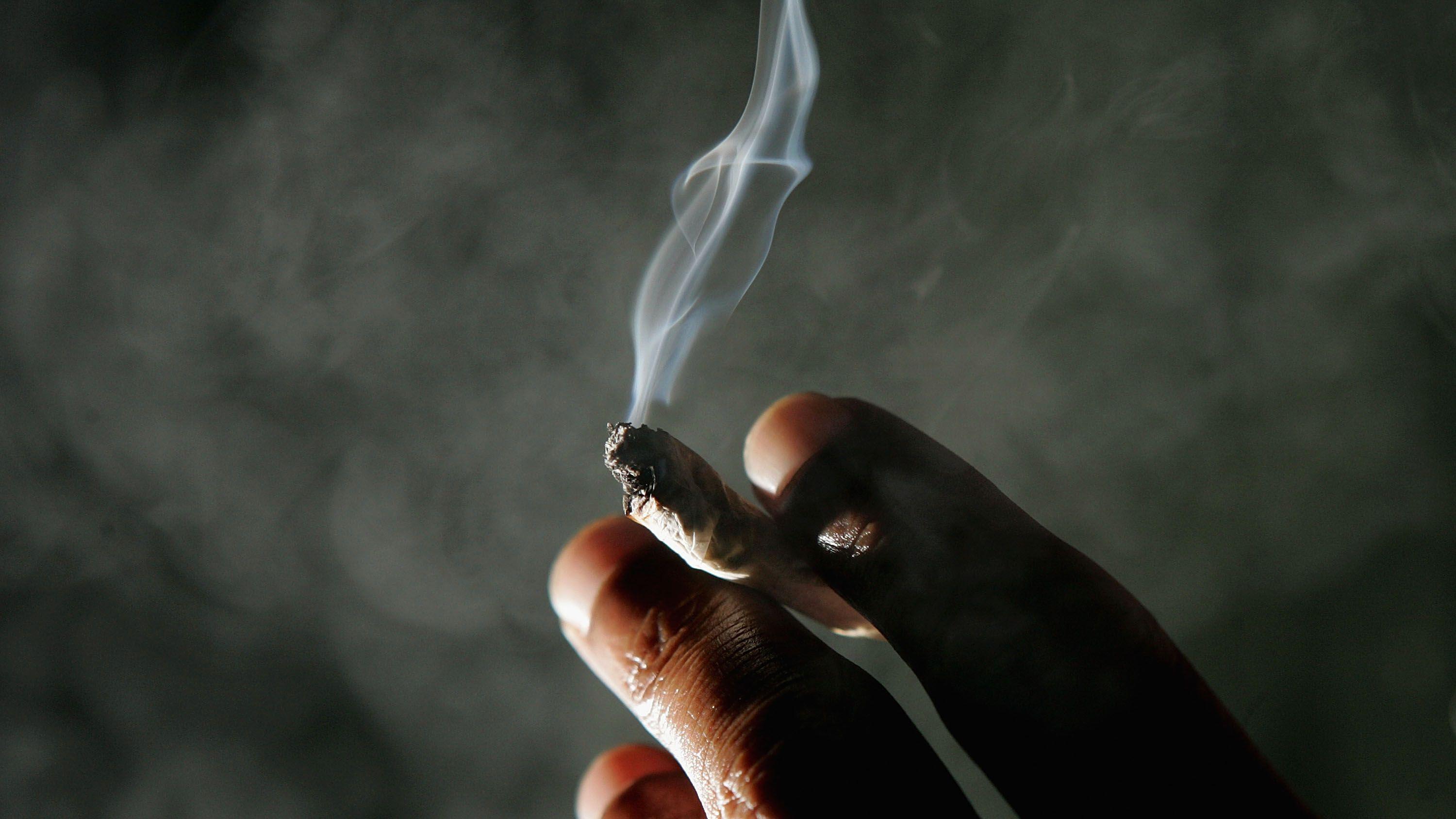 Image of someone's hand holding a lite marijuana cigarette 